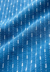 Țesătură textilă de culoare albastră vibrantă, cu un model repetitiv de dungi albe înguste, având o textură moale și un luciu subtil.