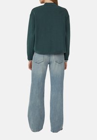 Grüner Sweatshirt mit rundem Halsausschnitt und langen Ärmeln, kombiniert mit hellblauen Schlagjeans mit Gesäßtaschen und einer ausgewaschenen Optik.