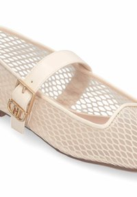 Chaussure plate Mary Jane en mesh beige avec une bride, une boucle dorée et un bout arrondi.