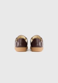 Par de zapatillas de cuero marrón oscuro con interior beige y suelas de goma marrón claro, vistas desde la parte trasera sobre fondo blanco.