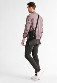 Borsa a tracolla nera, forma rettangolare, materiale resistente, presenta una tasca con zip, design minimalista e tracolla regolabile.