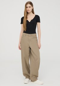 Pantaloni beige a gamba larga in cotone con vita alta, tasche frontali e chiusura a bottone, abbinati a un top fitted nero a maniche corte.