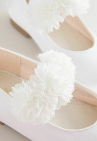 White ballet flats with textured, white fabric flowers on the front. Soft, smooth material and a rounded toe design, featuring a low heel.