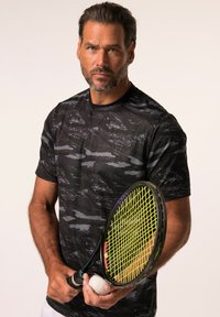 Zwart sport T-shirt met een gestructureerd grijs patroon, korte mouwen. Houdt een tennisracket vast met gele snaren en een witte tennisbal.