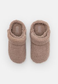 Pantoufles en polaire beige avec un col rabattu, texture douce et forme arrondie. La doublure intérieure correspond à la couleur extérieure.