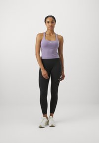 Lila sportos ujjatlan felső fekete leggingsszel párosítva. Simára varrt anyag, testhezálló fazon, kis logóval a mellkasán és a leggingsen.