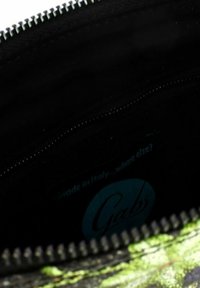 Interno di una pochette con zip, caratterizzato da un rivestimento in tessuto nero e un esterno con un motivo vivace verde e nero. Etichetta del marchio visibile all'interno.
