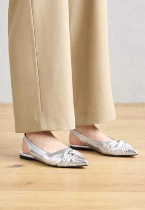 Hõbedased slingback madalad kingad, millel on sõlme detail varvaste juures, sile tekstuur, terav kuju ja madal konts, koos beežide laia säärega pükstega.