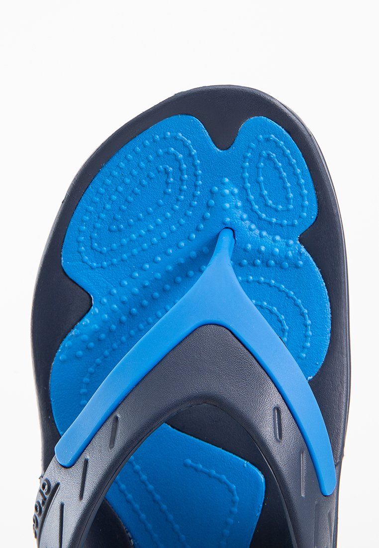 Blauwe en zwarte teenslipper met een textuur op de binnenzool en een driehoekige band. Heeft groeven en verhoogde stippen voor grip en comfort.