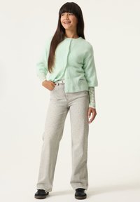 Cárdigan de manga corta verde menta con botones, combinado con jeans gris claro con estampado de lunares y calzado negro.