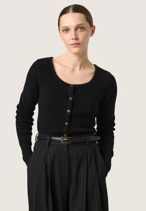 Black knitted cardigan with a scoop neckline, featuring gold-tone button closures and long sleeves. Style paired with black pinstripe trousers.