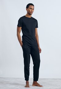 Tricou negru cu mânecă scurtă și pantaloni tapered asortați, confecționați dintr-un material moale. Design simplu cu o croială ajustată, purtat cu picioarele goale.