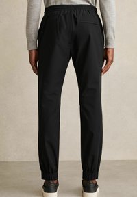 Black tapered joggers with an elastic waistband, featuring side pockets and ribbed cuffs. Smooth fabric with a sleek, minimalist design.