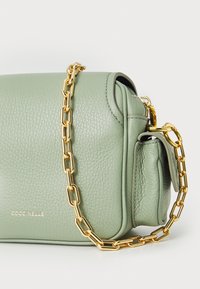 Sac à main en cuir vert avec une finition texturée, de forme rectangulaire et une chaîne en or. Logo "Coccinelle" présenté à l'avant.