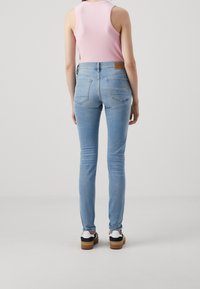 Ljusblå smala jeans med normal midja, bakfickor, ljusa sömdetaljer, i kombination med en rosa ärmlös topp och avslappnade skor.