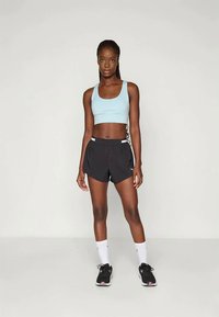 Gaiši zila sporta krūšturis apvienots ar melniem sporta šortiem ar baltu akcentu, valkāts ar melnām skriešanai paredzētām apavām un baltām zeķēm.