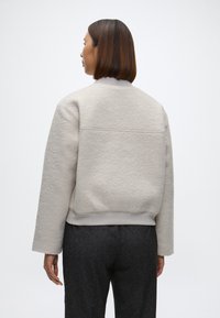 Lys grå teksturert bomberjakke med ribbet krage og mansjetter, som har en kortet design og en glatt innvendig fôr.