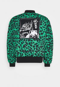 Veste bomber matelassée en vert vif avec imprimé léopard noir, ornée d'un patch graphique avec du texte audacieux et des motifs dans le dos.