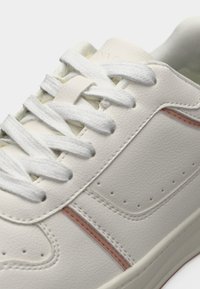 Gros plan d'une basket en cuir blanche avec des lacets blancs et des détails roses subtils le long du côté et des coutures.