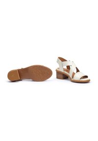White leather heeled sandals with crisscross straps and stitched accents, featuring a textured brown rubber sole and a stacked wooden heel.