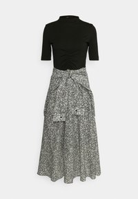 Top noir à manches courtes et coupe ajustée avec fronces à l'avant, associé à une longue jupe taille haute noire à motifs floraux blancs, ceinturée à la taille.