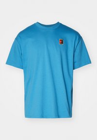 Blue cotton t-shirt with a crew neckline, short sleeves, and a small multicolored Nike logo patch on the chest. Smooth texture.