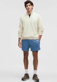 Felpa con zip crema, pantaloni shorts blu e sneakers marroni. Tessuto morbido, vestibilità rilassata, polsini a coste e tasche laterali sui pantaloni shorts.