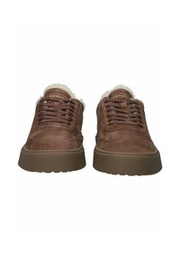 Bruine suede sneakers met een gestructureerd oppervlak, rubberen zolen en een zachte witte bontvoering rond de enkel. Veters en merk zichtbaar.