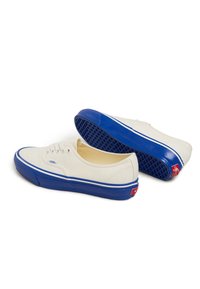Canvas sneakers in crème met blauwe rubberen zolen. Kenmerken zijn onder andere een witte vetersluiting, blauwe accenten en een gestructureerde buitenzool.