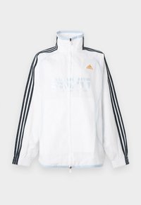 Λευκό μπουφάν Adidas με φερμουάρ και ψηλό γιακά, μαύρα μανίκια με τρεις ρίγες και πορτοκαλί λογότυπο στο στήθος.