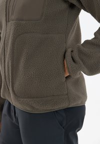 Fleece jacket in dark gray with a textured surface, featuring a zip pocket and elastic cuffs, paired with navy pants.