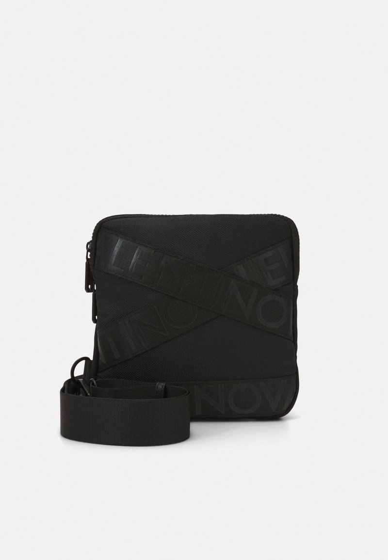 Black crossbody bag featuring a textured fabric, zip closure, and a bold logo pattern across the front. Includes a matching strap.