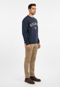 Sudadera marinera con el logo "SILBO" en color beige, combinada con pantalones color beige y botines marrones. Diseño simple con puños acanalados y bajo.