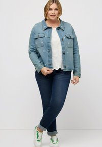 Světle modrá džísková bunda s vyšívanými květinami, bílý krajkový top, tmavé džíny a bílé tenisky s zelenými akcenty. Neformální outfit.