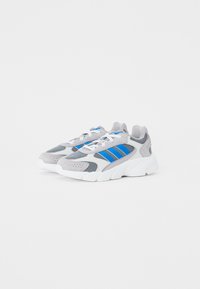 Zapatillas deportivas grises con parte superior de malla y gamuza, acentos de tres rayas azules, suela blanca y cordones blancos.
