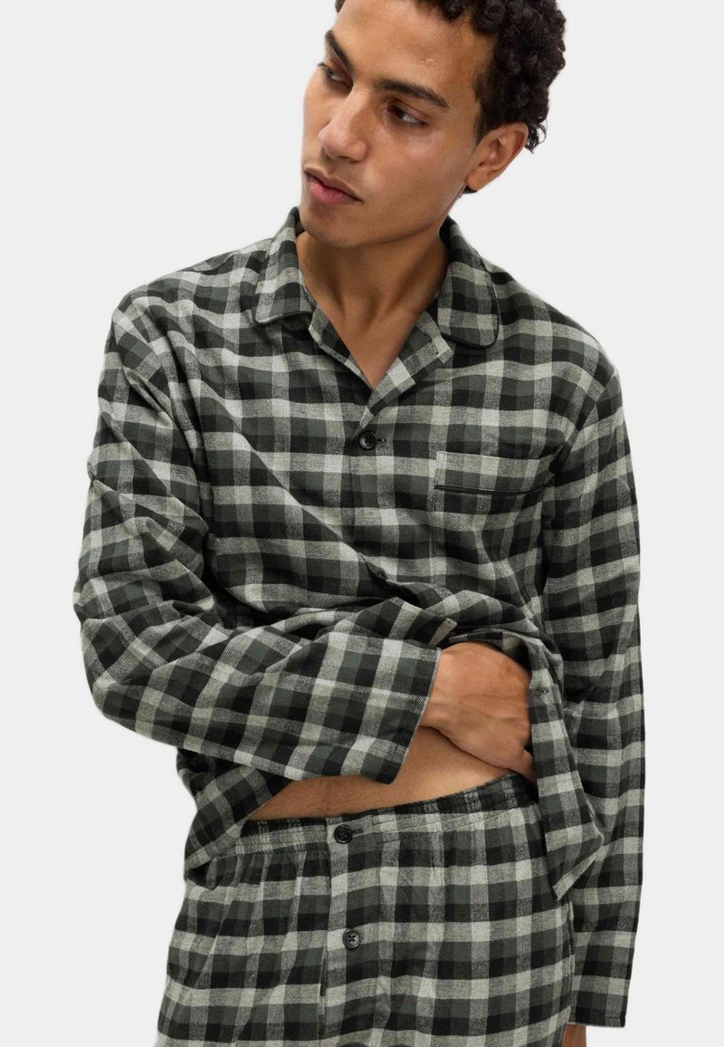 Conjunto de pijama a cuadros en negro y gris, hecho de tela suave. Camisa de manga larga con un bolsillo en el pecho, puños abotonados y pantalones a juego con botones.