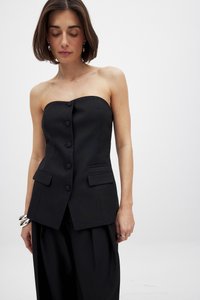 Musta olkaimeton paita, joka on valmistettu sileästä kankaasta. Siinä on kuusi etunappia ja kaksi sivutaskua, sekä muotoiltu malli ja jämäkkä siluetti.