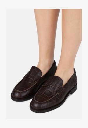 Mocasines de cuero marrón oscuro con textura de cocodrilo, que presentan una suela plana y costuras de acento en la parte superior.