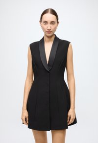 Black sleeveless dress with a deep V-neck, satin lapel, fitted bodice, and flared skirt. Smooth fabric with subtle seams and no visible hardware.