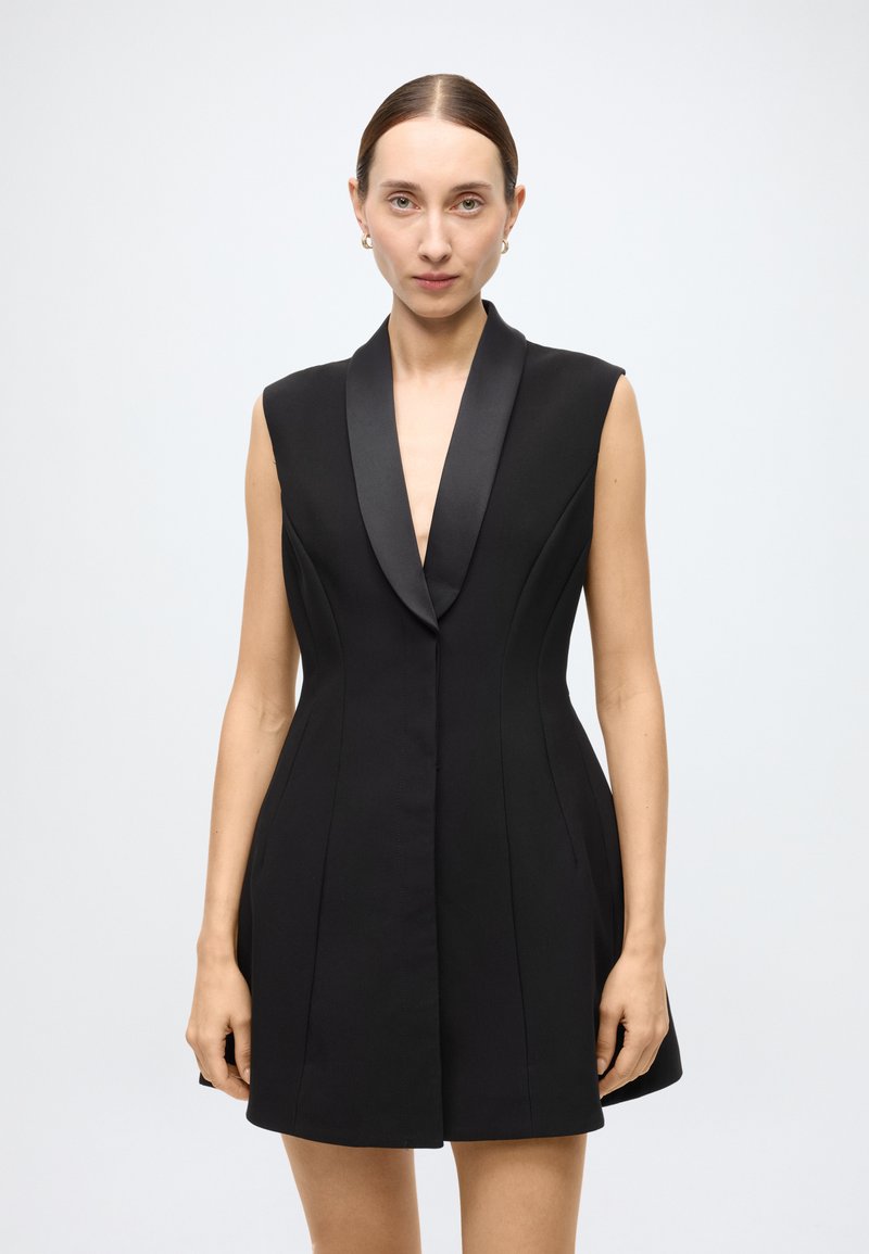 Black sleeveless dress with a deep V-neck, satin lapel, fitted bodice, and flared skirt. Smooth fabric with subtle seams and no visible hardware.