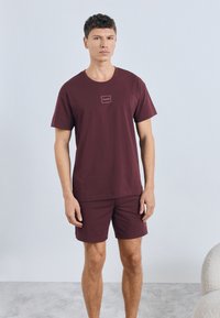 Βουργουνδίας βαμβακερό κοντομάνικο μπλουζάκι με διακριτικό λογότυπο στο στήθος, σετ με αντίστοιχα σορτς, και τα δύο με άνετη εφαρμογή.