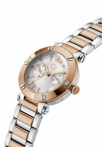 Orologio in acciaio inox rosé e argento con quadrante bianco testurizzato, grandi numeri romani, due sotto-quadranti e cassa rotonda con dettagli decorativi.