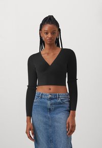 Schwarzes, geripptes Langarm-Crop-Top mit tiefem V-Ausschnitt, kombiniert mit einem hochtaillierten blauen Jeansrock. Texturiertes Material, figurbetonte Silhouette.