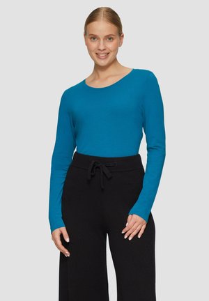 Lange mouw top in fel teal stof met een ronde halslijn, gecombineerd met zwarte broek met trekkoord. Glad textuur, aansluitend ontwerp.