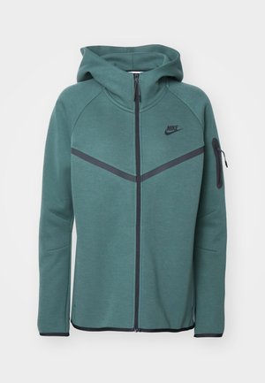 Felpa verde con zip, cappuccio, accenti neri diagonali, logo Nike sul petto e tasca laterale con zip. Realizzata in tessuto testurizzato.