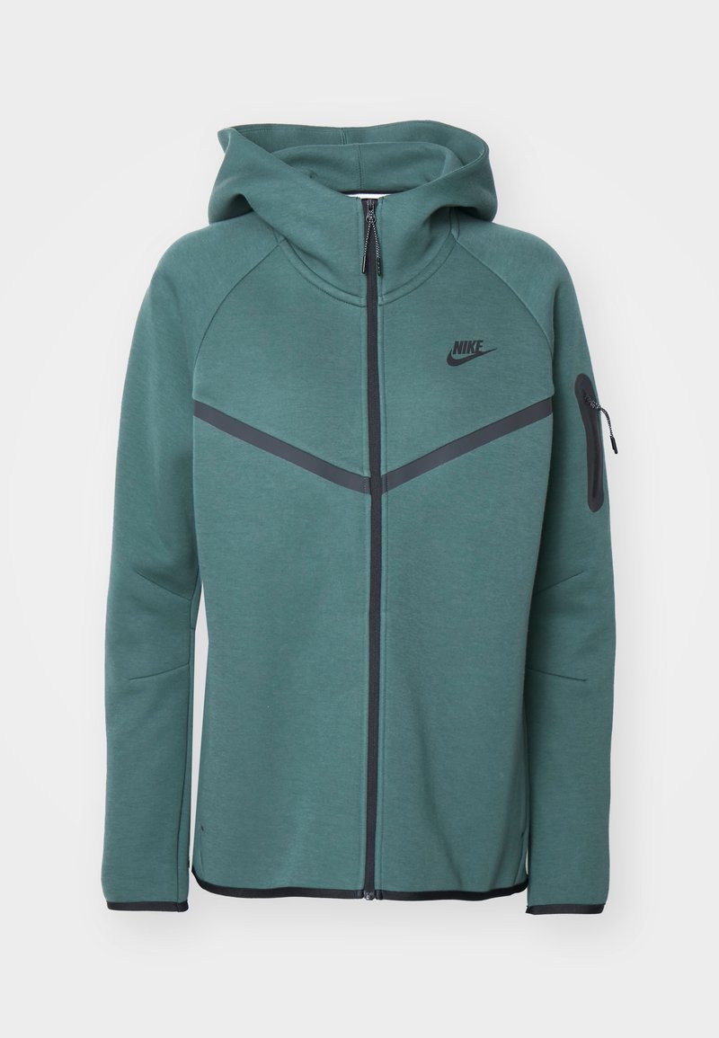 Haut zippé vert avec capuche, accents noirs en diagonale, logo Nike sur la poitrine et une poche latérale zippée. Fabriqué en tissu texturé.