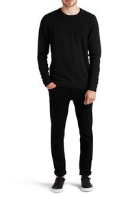 Czarny sweter z dzianiny z prążkowanym wzorem na ramionach i prostym krojem. Zestawiony z dopasowanymi czarnymi spodniami i casualowymi czarnymi sneakersami.