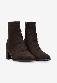 Stivaletti alla caviglia in camoscio marrone con un design morbido, punta appuntita e zip laterale. Presentano un tacco a blocco per una maggiore stabilità.