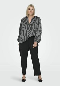 Grå satinblus med V-ringning och zebramönster, kombinerad med svarta tapered byxor och svarta ballerinaskor. Mjuk textur och lös passform.