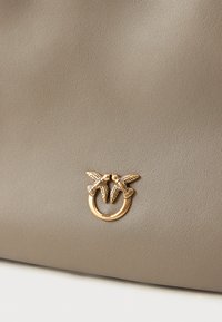 Taupe-Lederoberfläche mit einem kleinen goldenen Ringdetail, das zwei kunstvoll gestaltete Vögel zeigt, die sich in der Mitte mit den Schnäbeln berühren.